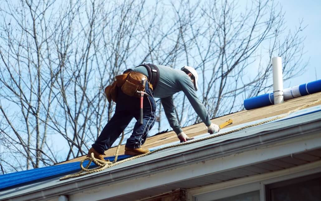 Man climbing on residential rooftop making repairs