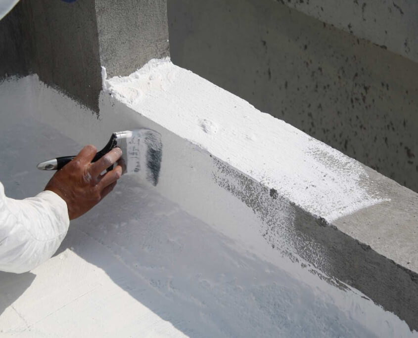 Man using paint brush to apply waterproofing substance to edges of a flat top commercial roof
