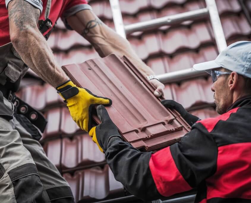 Men working together to pass shingles up to workers on top of a home