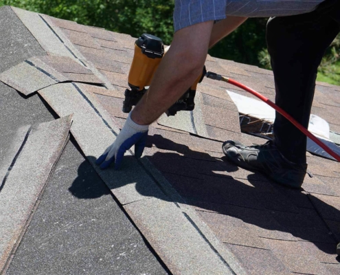 Roofer using a nail gun to nail in shingles on a roof replacement