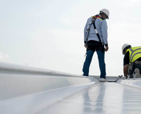 two roofers performing routine inspection on top of roof