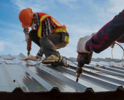 Two roofers laying metal on roof surface, using tools