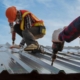 Two roofers laying metal on roof surface, using tools